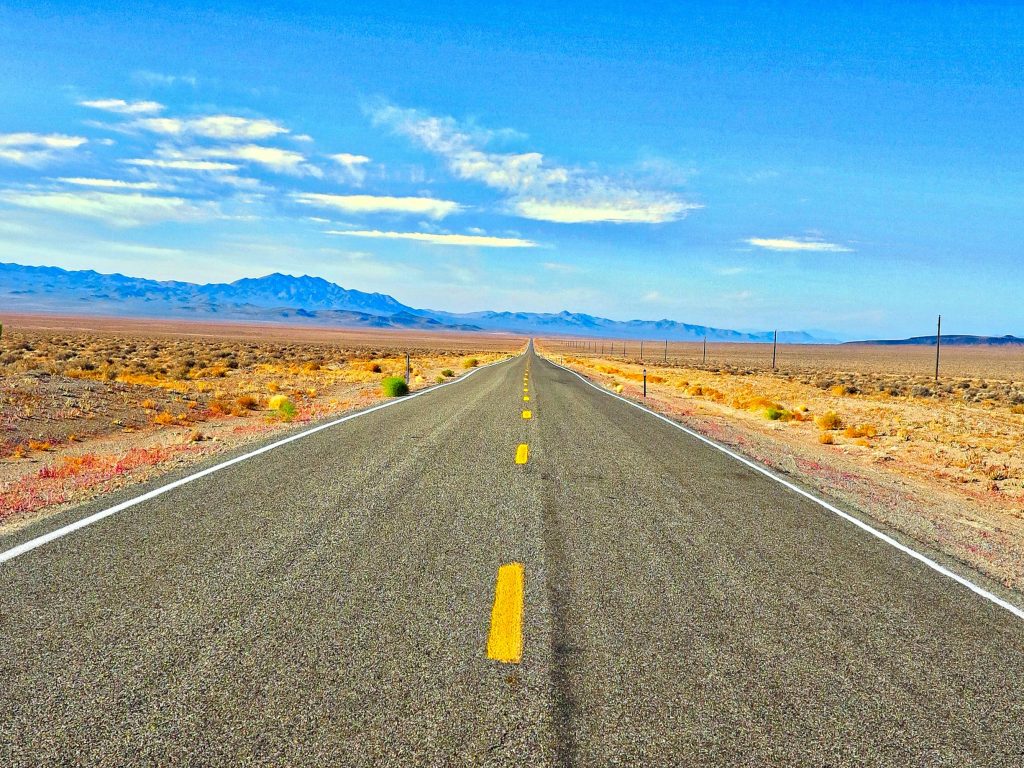 A long straight road in the Nevada desert under a blue sky, perfect for travel and adventure.